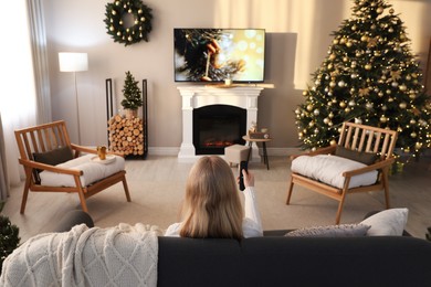 Woman on sofa watching TV in room decorated for Christmas, back view