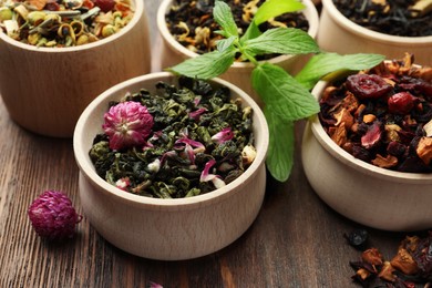 Photo of Different kinds of dry herbal tea in bowls on wooden table