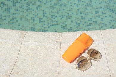 Stylish sunglasses and sunscreen near outdoor swimming pool on sunny day, space for text. Beach accessories