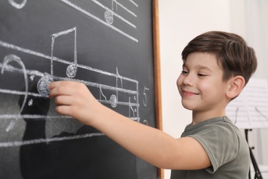 Little boy writing music notes on blackboard in classroom