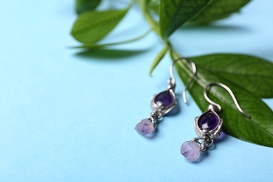 Beautiful pair of silver earrings with amethyst gemstones and leaves on light blue background, closeup. Space for text