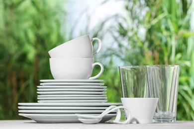 Photo of Set of clean dishware on white table against blurred background