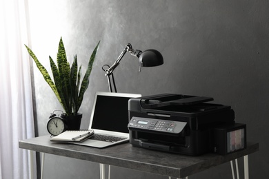 Photo of New modern printer and laptop on grey table in office