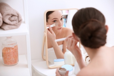 Woman applying scrub onto face in front of mirror at home