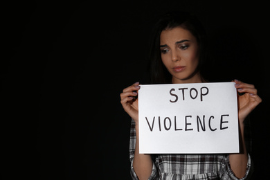 Photo of Abused young woman with sign STOP VIOLENCE on black background, space for text