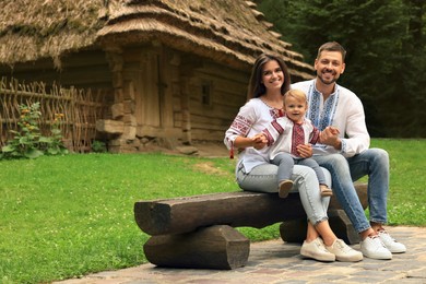 Happy family in Ukrainian national clothes sitting on bench outdoors