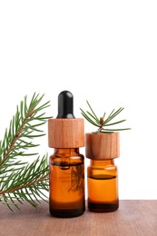 Photo of Bottles of pine essential oil and tree branch on wooden table against white background