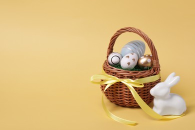 Photo of Easter basket with painted eggs and figure of rabbit on yellow background. Space for text