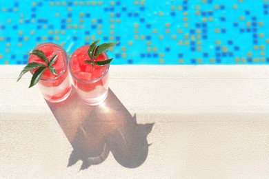 Refreshing watermelon drink in glasses near swimming pool outdoors, top view. Space for text