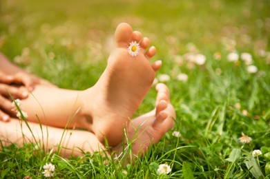 Child with chamomile between toes sitting on green grass outdoors, closeup of feet