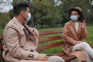 Man and woman talking on bench in park. Keeping social distance during coronavirus pandemic