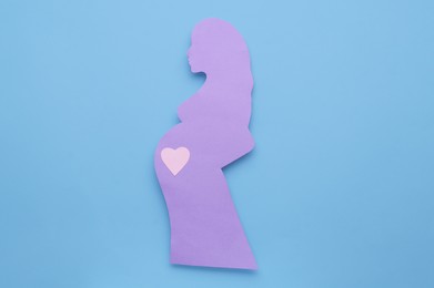 Photo of Pregnant woman with heart on belly on light blue background, top view