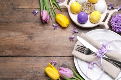 Festive Easter table setting with painted eggs and flowers on wooden background, flat lay. Space for text