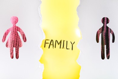 Photo of Divorce concept. Balloon with word Family between man and woman silhouettes, view through holes in white paper