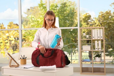 Businesswoman packing sports stuff for training into bag in office