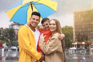 Happy family with umbrella walking under rain on city street