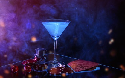 Casino chips, dice, playing cards and cocktail on dark background with smoke