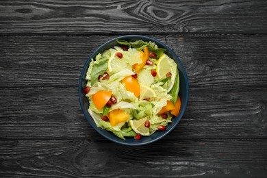 Photo of Delicious salad with Chinese cabbage, lemon, persimmon and pomegranate seeds on black wooden table, top view