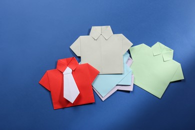 Photo of Many paper shirts on blue background, flat lay. Recruiter searching employee