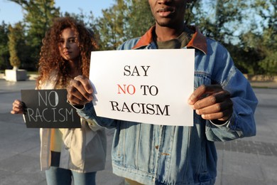African American woman and man holding signs with phrase Say No To Racism outdoors, closeup