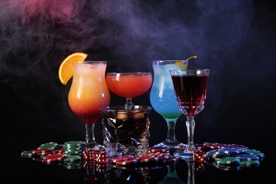 Casino chips, dice and alcohol drinks on dark background with smoke