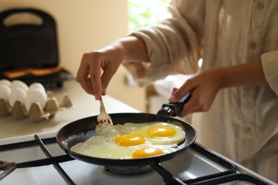 Woman cooking tasty eggs on frying pan in kitchen, closeup
