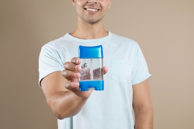 Young man holding deodorant on beige background, closeup. Mockup for design