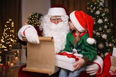 Little girl with Christmas gift near Santa Claus indoors