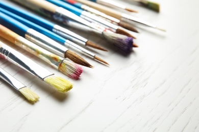 Different paint brushes on wooden table, closeup. Space for text