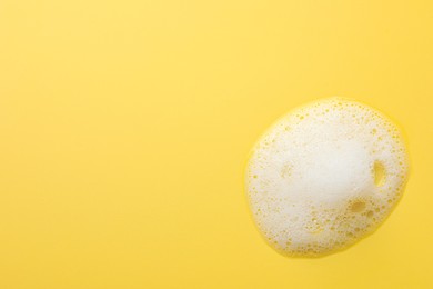 Fluffy soap foam on yellow background, top view. Space for text