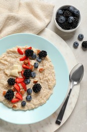 Tasty oatmeal porridge with berries and almond nuts served on light table, flat lay