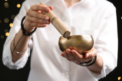 Woman using singing bowl in sound healing therapy on black background, closeup