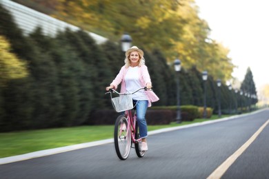 Image of Mature woman riding bicycle outdoors, motion blur effect