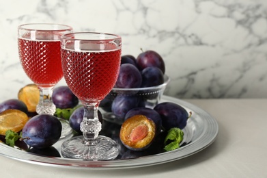 Delicious plum liquor, mint and ripe fruits on white table. Homemade strong alcoholic beverage