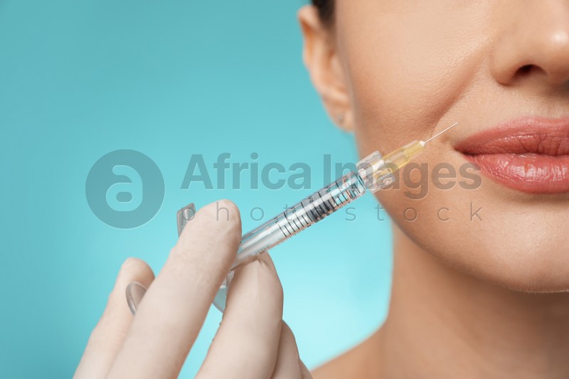 Beautiful woman getting facial injection on light blue background, closeup. Cosmetic surgery