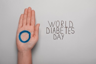 Woman showing palm with blue circle near text World Diabetes Day on light background, closeup