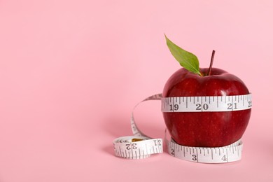 Fresh red apple with measuring tape on pink background. Space for text