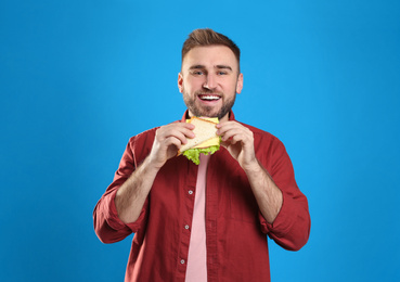Photo of Young man with tasty sandwich on light blue background