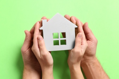 Couple holding house model on light green background, top view