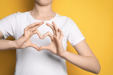 Woman making heart with hands on yellow background, closeup