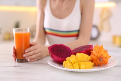 Photo of Woman with fresh juice and exotic fruits at table in kitchen, closeup