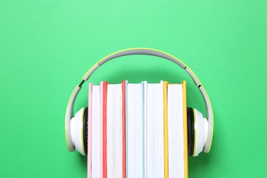 Photo of Books with modern headphones on green background, top view