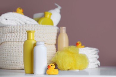 Bottles of baby cosmetic products and rubber duck on white table. Space for text