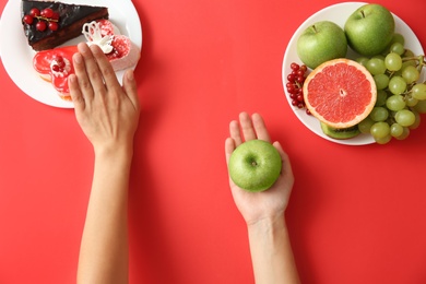 Top view of woman choosing between sweets and healthy fruits on red background, closeup