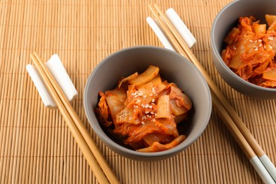 Bowls of spicy cabbage kimchi and chopsticks on bamboo mat