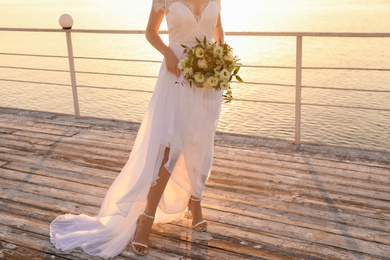 Bride in beautiful wedding dress with bouquet near river on sunset, closeup