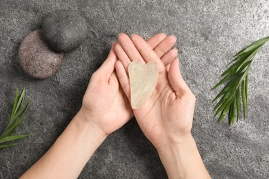 Photo of Woman holding gua sha tool over grey stone table, top view