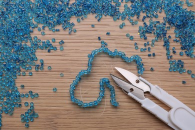Bright light blue glass beads, bracelet and scissors on wooden table, flat lay