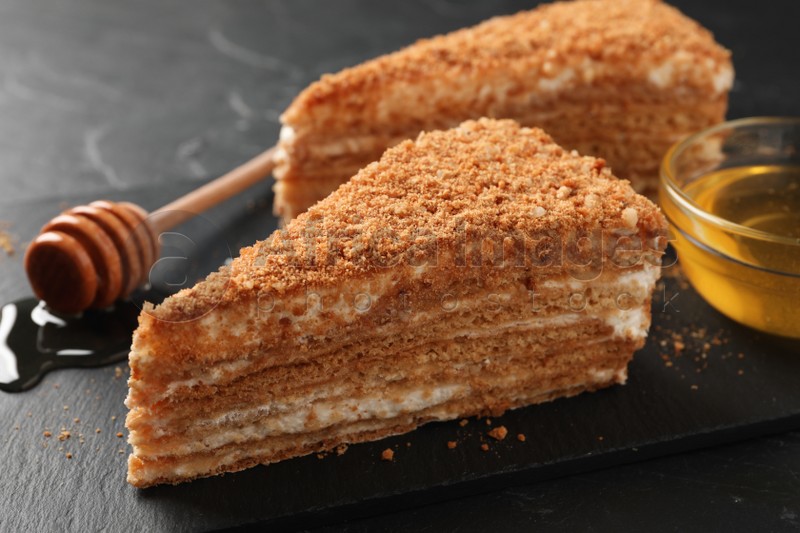 Slices of delicious layered honey cake served on black table, closeup