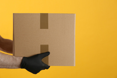 Courier holding cardboard box on yellow background, closeup. Parcel delivery